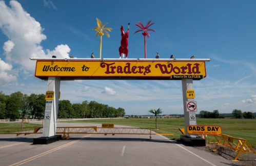 A colorful archway sign welcomes visitors to Traders World, featuring palm trees and a red rabbit statue.