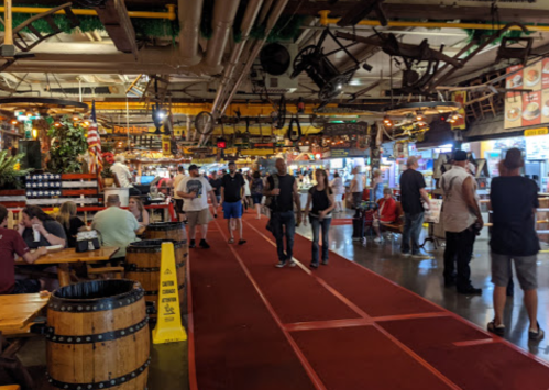 A bustling indoor market with people dining and shopping, featuring colorful stalls and festive decorations.