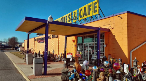 Colorful storefront of a cafe and antiques shop, featuring various decorative items in front. Bright blue sky above.