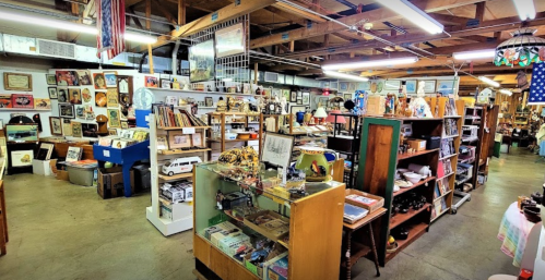 A spacious antique shop filled with various collectibles, furniture, and framed art on display.