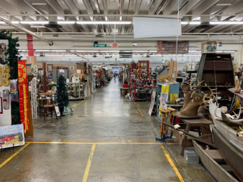 A spacious antique shop aisle lined with various vintage items, furniture, and decorations on both sides.