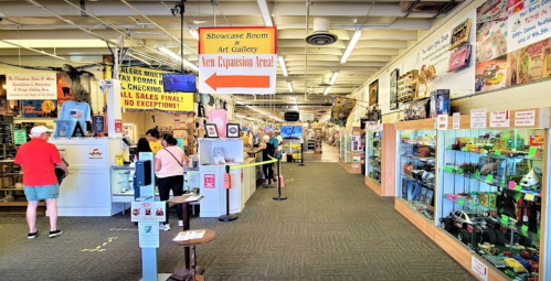 A bustling indoor market with various displays, art gallery signs, and shoppers exploring different booths.