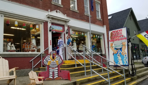 A storefront with colorful decorations, featuring a mannequin in a striped outfit and a sign for a prison showroom.