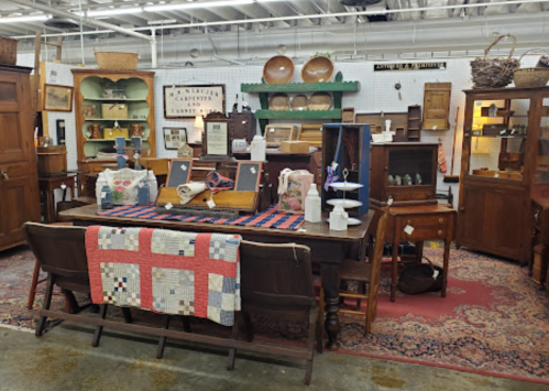 A vintage shop display featuring wooden furniture, quilts, and various antique items arranged on tables and shelves.