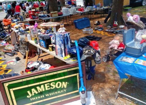 A bustling flea market scene with various items for sale, including toys, tools, and a Jameson Irish Whiskey sign.