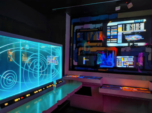 Futuristic control room with glowing screens, a holographic display, and colorful interface elements.