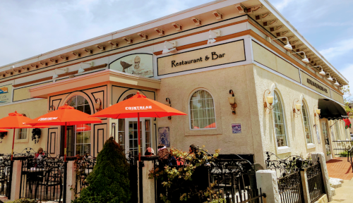 A charming restaurant and bar with outdoor seating, featuring red umbrellas and decorative architecture.