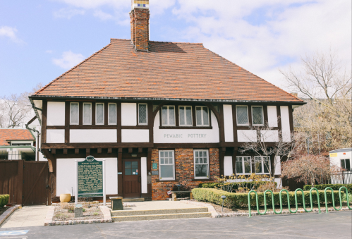 A charming two-story building with a brick and timber facade, featuring a sign for "Pewabic Pottery" and a landscaped entrance.