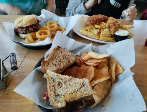 A table with three plates: a sandwich with chips, onion rings, and a plate of fries with chicken tenders and dipping sauce.