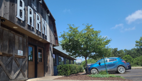 Exterior view of "The Barn" restaurant, featuring a wooden facade, a blue car parked, and clear blue skies.