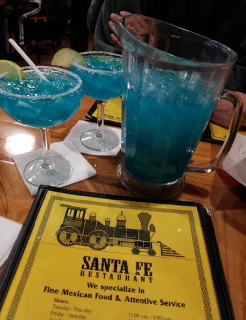 Two blue cocktails with lime slices and a pitcher on a table with a menu for Santa Fe Restaurant.