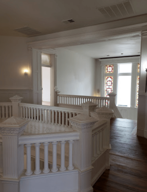 Interior view of a bright, spacious hallway with ornate white railings and stained glass windows.