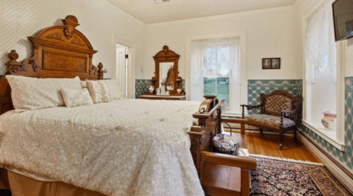 Cozy bedroom featuring a large bed, vintage furniture, and decorative wallpaper in soft colors.