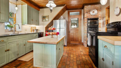 Cozy kitchen with mint green cabinets, a wooden island, brick accents, and stainless steel appliances.