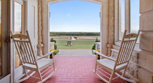 Two white rocking chairs on a porch, overlooking a scenic view of a green landscape and blue sky.