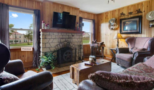 Cozy living room with wooden walls, a stone fireplace, and comfortable seating, featuring a TV and decorative items.