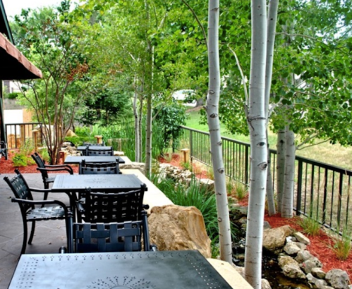 Outdoor patio with black tables and chairs, surrounded by greenery and trees, featuring a small rock garden.