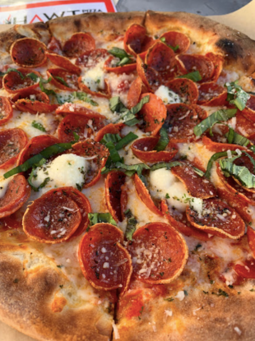 A close-up of a pepperoni pizza topped with fresh basil and cheese, showcasing a golden crust and vibrant toppings.