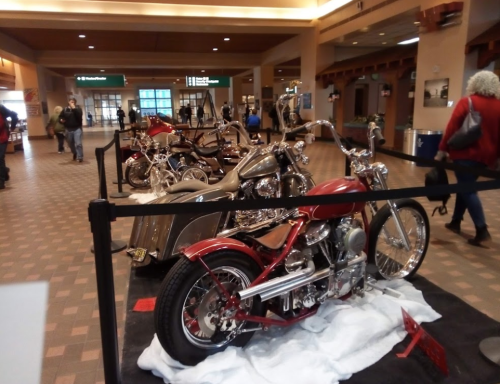 A display of custom motorcycles in an airport terminal, with various styles and colors showcased.