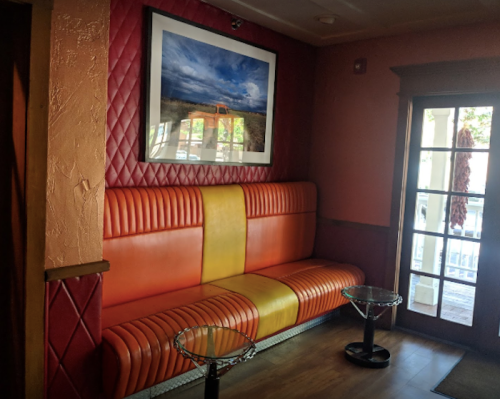 A cozy seating area with an orange and yellow bench, framed artwork on the wall, and glass side tables.