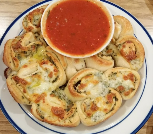 A plate of cheesy garlic rolls arranged around a bowl of marinara sauce.