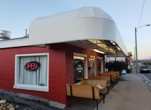 A small restaurant with a red exterior, an "OPEN" sign, and outdoor seating along the sidewalk.