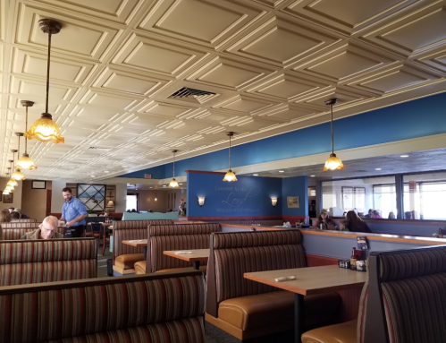 Interior of a diner with striped booths, pendant lights, and a blue accent wall. Customers are seated and a server is visible.