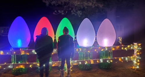Two people stand in front of large, illuminated egg-shaped decorations, surrounded by string lights at night.