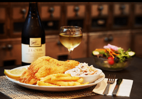 A plate of fried fish with fries and coleslaw, accompanied by a glass of white wine and a side salad.