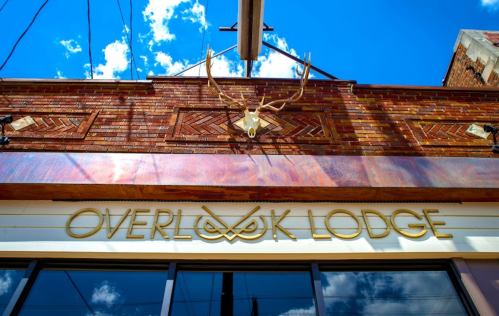 Sign for Overlook Lodge with antlers above it, set against a bright blue sky with scattered clouds.