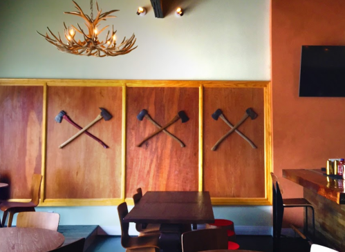 Interior of a restaurant featuring wooden walls with crossed axes and an antler chandelier above.