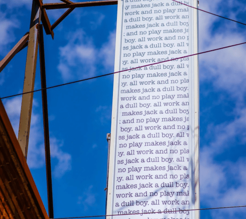 A tall structure with a banner displaying repeated text about "Jack" and the phrase "all work and no play." Blue sky in background.