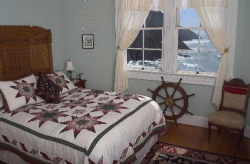 Cozy bedroom with a quilted bed, nautical decor, and a view of the ocean through large windows.
