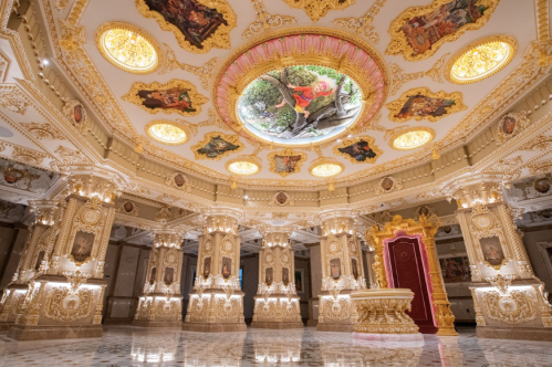 Opulent interior featuring ornate columns, a colorful ceiling mural, and intricate gold detailing in a grand hall.