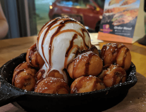 A skillet filled with warm doughnut holes topped with vanilla ice cream and drizzled with chocolate sauce.