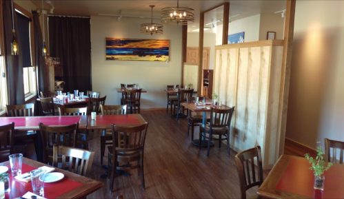 A cozy restaurant interior with wooden tables, chairs, and a colorful painting on the wall.