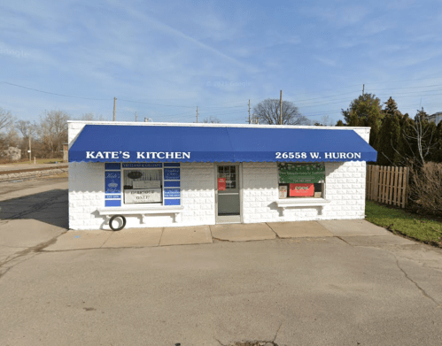 A small white building with a blue awning reading "Kate's Kitchen" and a sign displaying the address.