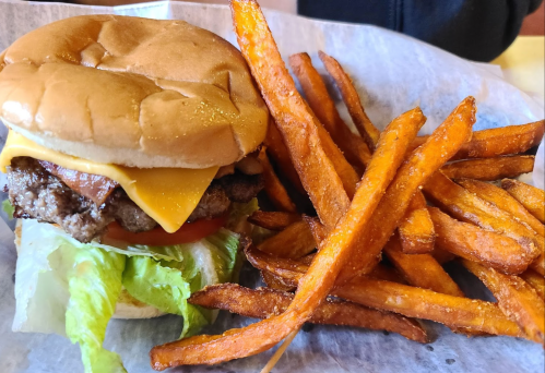A cheeseburger with lettuce, tomato, and a side of crispy sweet potato fries on a paper-lined plate.