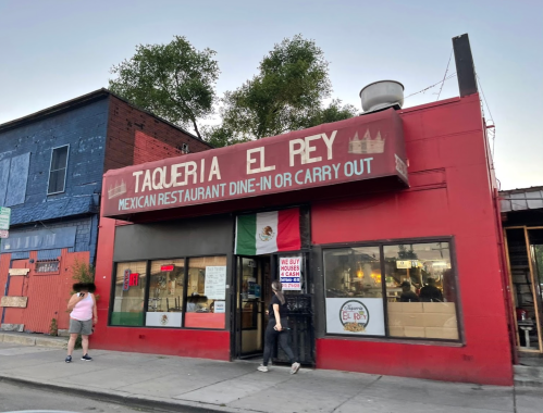 A red building with a sign reading "Taqueria El Rey," featuring a Mexican flag and a person entering the restaurant.