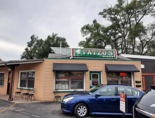 Exterior of Fatzo's Pizza, a small restaurant with a sign and outdoor seating, under a cloudy sky.