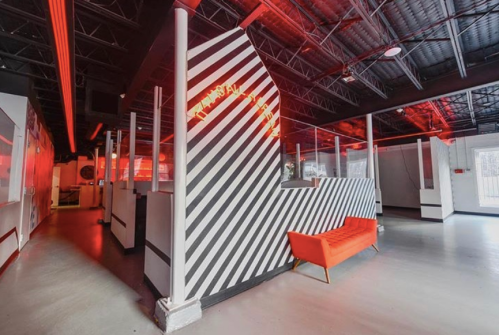 Interior of a modern space featuring red lighting, striped walls, and a bright orange couch.