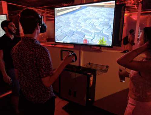 A group of people enjoying a virtual reality game in a dimly lit room with a large screen displaying the game.