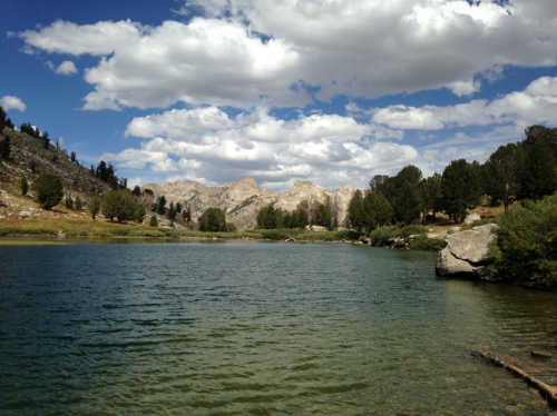 A serene lake surrounded by mountains and trees under a partly cloudy sky.