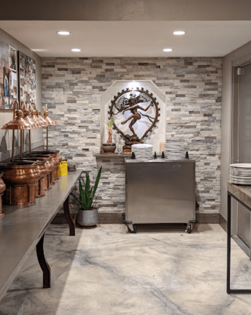 A modern dining area featuring copper serving dishes, a decorative wall, and a statue of a dancer against a stone backdrop.