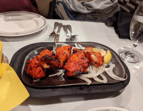 A sizzling platter of grilled chicken pieces with onions and a lemon wedge, served on a black plate.