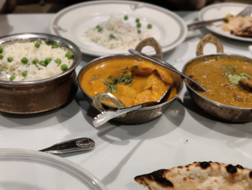 A table setting with bowls of rice, curry, and naan bread, featuring vibrant yellow and orange dishes with garnishes.