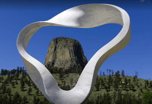 A sculptural frame in the foreground highlights the iconic Devil's Tower against a clear blue sky.