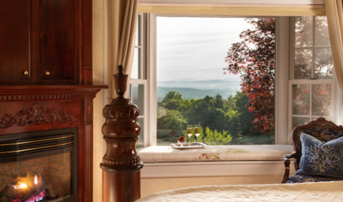 Cozy bedroom with a fireplace and a scenic view of mountains through a large window.