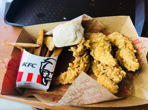 A tray with KFC chicken tenders, a biscuit, and a side of fries in a branded container.