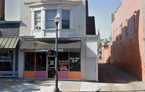 A small bakery with a colorful sign, featuring a drive-thru, next to a narrow alleyway.